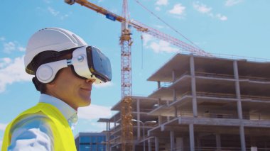 İnşaat alanının önünde sanal gerçeklik teknolojileri kullanarak VR kasklı profesyonel bir inşaatçı. Ofis binası ve vinç arka planı. Emlak ve yatırım kavramları