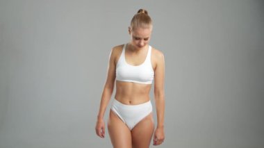 Genç, fit ve beyaz mayo giymiş güzel sarışın kadın gri arka planda poz veriyor. Sağlık, diyet, spor ve spor kavramı.