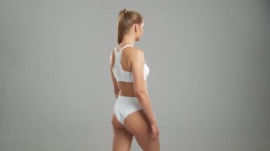 Genç, fit ve beyaz mayo giymiş güzel sarışın kadın gri arka planda poz veriyor. Sağlık, diyet, spor ve spor kavramı.
