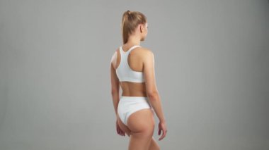 Genç, fit ve beyaz mayo giymiş güzel sarışın kadın gri arka planda poz veriyor. Sağlık, diyet, spor ve spor kavramı.