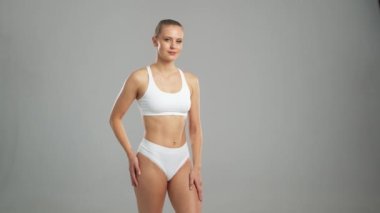Genç, fit ve beyaz mayo giymiş güzel sarışın kadın gri arka planda poz veriyor. Sağlık, diyet, spor ve spor kavramı.