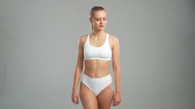 Genç, fit ve beyaz mayo giymiş güzel sarışın kadın gri arka planda poz veriyor. Sağlık, diyet, spor ve spor kavramı.