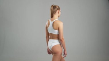 Genç, fit ve beyaz mayo giymiş güzel sarışın kadın gri arka planda poz veriyor. Sağlık, diyet, spor ve spor kavramı.