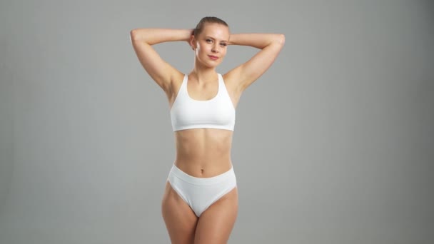 グレーの背景に白い水着姿の若い フィット感のある美しい金髪の女性 ヘルスケア スポーツ フィットネスの概念 — ストック動画