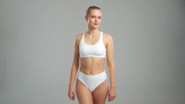 Genç, fit ve beyaz mayo giymiş güzel sarışın kadın gri arka planda poz veriyor. Sağlık, diyet, spor ve spor kavramı.