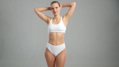 Genç, fit ve beyaz mayo giymiş güzel sarışın kadın gri arka planda poz veriyor. Sağlık, diyet, spor ve spor kavramı.