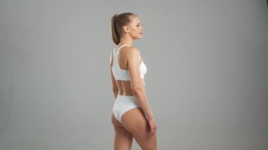 Genç, fit ve beyaz mayo giymiş güzel sarışın kadın gri arka planda poz veriyor. Sağlık, diyet, spor ve spor kavramı.
