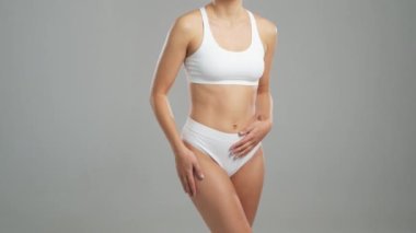 Genç, fit ve beyaz mayo giymiş güzel sarışın kadın gri arka planda poz veriyor. Sağlık, diyet, spor ve spor kavramı.