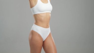Genç, fit ve beyaz mayo giymiş güzel sarışın kadın gri arka planda poz veriyor. Sağlık, diyet, spor ve spor kavramı.