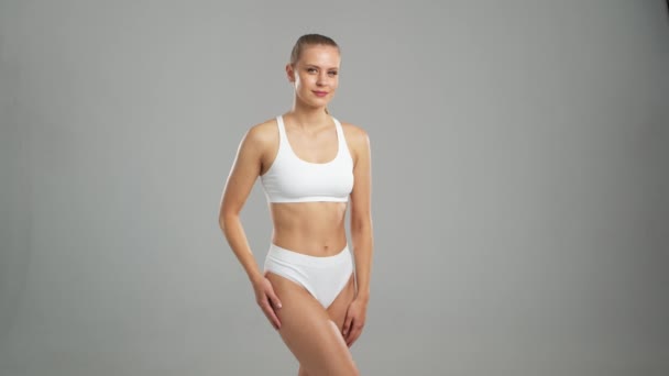 グレーの背景に白い水着姿の若い フィット感のある美しい金髪の女性 ヘルスケア スポーツ フィットネスの概念 — ストック動画