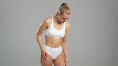 Genç, fit ve beyaz mayo giymiş güzel sarışın kadın gri arka planda poz veriyor. Sağlık, diyet, spor ve spor kavramı.