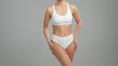 Genç, fit ve beyaz mayo giymiş güzel sarışın kadın gri arka planda poz veriyor. Sağlık, diyet, spor ve spor kavramı.