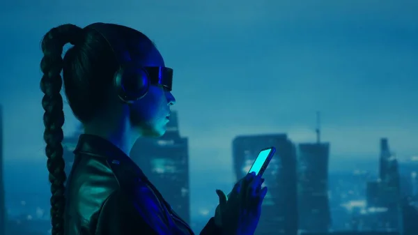 メガネやヘッドフォンでスマートフォンとサイバーパンクの女の子の肖像画 都市の高層ビルの背景に美しい若い女性 未来的概念 — ストック写真