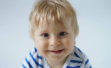 Stüdyoda küçük, mutlu ve gülümseyen bir bebek. Bir yaşındaki bir bebeğin portresi. Gri arka plan. Mutluluk kavramı.