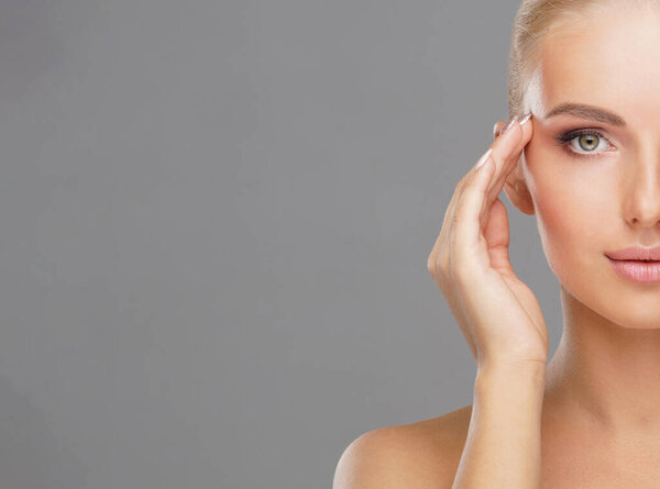 Beautiful face of young and healthy girl over grey background. Skin care, cosmetics and face lifting concept.
