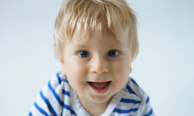 Stüdyoda küçük, mutlu ve gülümseyen bir bebek. Bir yaşındaki bir bebeğin portresi. Gri arka plan. Mutluluk kavramı.