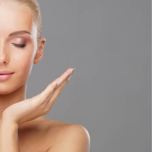 Beautiful face of young and healthy girl over grey background. Skin care, cosmetics and face lifting concept.