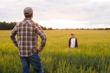 Çiftçi ve oğlu günbatımı tarımının önünde. Kırsalda bir adam ve bir çocuk. Babalık kavramı, köy hayatı, tarım ve kırsal yaşam tarzı..