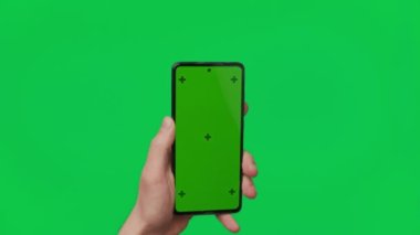 Male hand holding a smartphone with vertical green chroma key screen isolated on green background. Mobile phone in a hand. Different signs and gestures with fingers. 4K template. Technology and