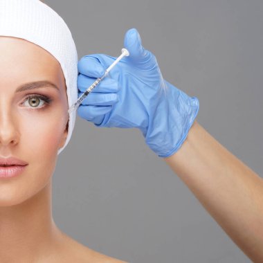 Genç bir kadının güzel yüzüne iğne yapan bir doktor. Estetik ameliyat, cilt gerdirme ve estetik tıp konsepti.