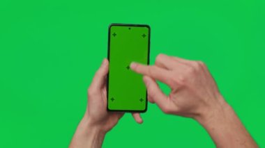 Male hand holding a smartphone with vertical green chroma key screen isolated on green background. Mobile phone in a hand. Different signs and gestures with fingers. 4K template. Technology and