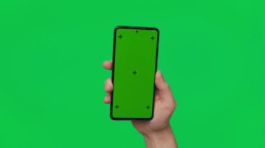 Male hand holding a smartphone with vertical green chroma key screen isolated on green background. Mobile phone in a hand. Different signs and gestures with fingers. 4K template. Technology and