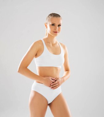 Young, fit and beautiful blond woman in white swimsuit isolated on grey background. The concept of healthcare, diet, sport and fitness.