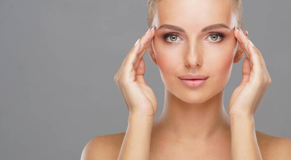 Beautiful face of young and healthy girl over grey background. Skin care, cosmetics and face lifting concept.