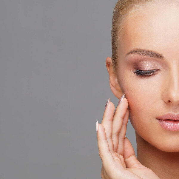 Beautiful face of young and healthy girl over grey background. Skin care, cosmetics and face lifting concept.