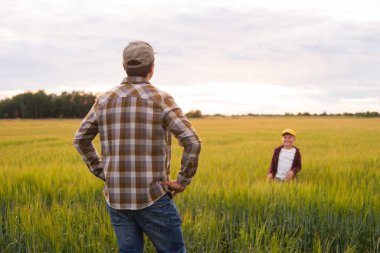 Çiftçi ve oğlu günbatımı tarımının önünde. Kırsalda bir adam ve bir çocuk. Babalık kavramı, köy hayatı, tarım ve kırsal yaşam tarzı..