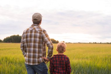 Çiftçi ve oğlu günbatımı tarımının önünde. Kırsalda bir adam ve bir çocuk. Babalık kavramı, köy hayatı, tarım ve kırsal yaşam tarzı..