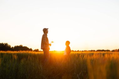 Farmer and his son in front of a sunset agricultural landscape. Man and a boy in a countryside field. The concept of fatherhood, country life, farming and country lifestyle.