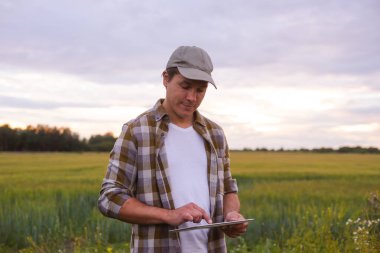 Farmer with a tablet computer in front of a sunset agricultural landscape. Man in a countryside field. The concept of country life, food production, farming and technology.