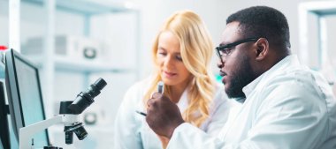 Laboratuvarda çalışan tıp bilimcileri. Doktor stajyerlere araştırma yapmayı öğretiyor. Laboratuvar aletleri: mikroskop, test tüpleri, ekipmanlar. Biyoteknoloji, bakteriyoloji, viroloji ve sağlık hizmetleri kavramı.