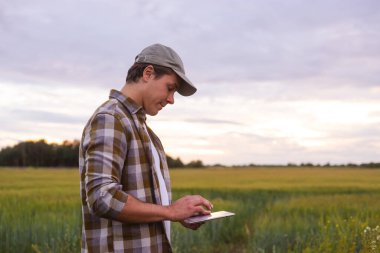 Farmer with a tablet computer in front of a sunset agricultural landscape. Man in a countryside field. The concept of country life, food production, farming and technology.