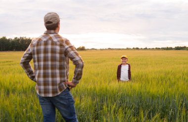 Çiftçi ve oğlu günbatımı tarımının önünde. Kırsalda bir adam ve bir çocuk. Babalık kavramı, köy hayatı, tarım ve kırsal yaşam tarzı..
