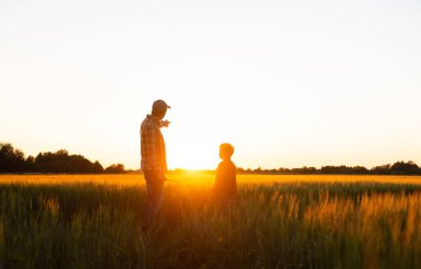 Farmer and his son in front of a sunset agricultural landscape. Man and a boy in a countryside field. The concept of fatherhood, country life, farming and country lifestyle.