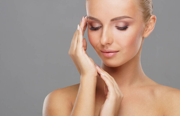 Beautiful face of young and healthy girl over grey background. Skin care, cosmetics and face lifting concept.