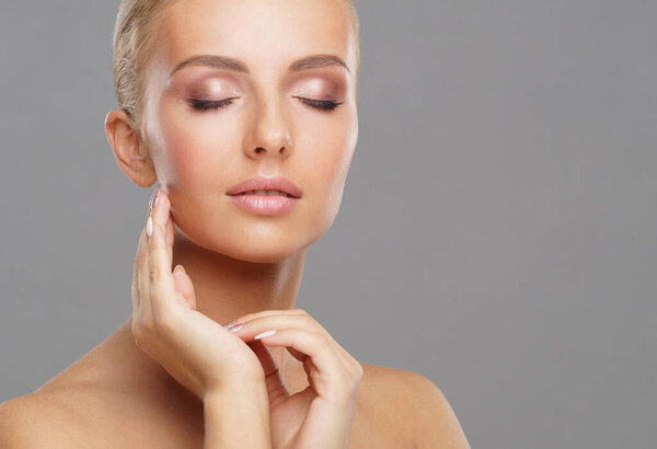 Beautiful face of young and healthy girl over grey background. Skin care, cosmetics and face lifting concept.