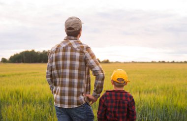 Farmer and his son in front of a sunset agricultural landscape. Man and a boy in a countryside field. The concept of fatherhood, country life, farming and country lifestyle. clipart