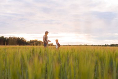 Farmer and his son in front of a sunset agricultural landscape. Man and a boy in a countryside field. The concept of fatherhood, country life, farming and country lifestyle.