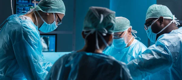 医療従事者の多様なチームは ハイテク機器と技術を使用して現代の手術室で外科手術を行います 外科医は病院で患者を救うために働いている — ストック写真