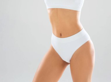 Beyaz mayo giymiş, beyaz arka planda poz veren genç ve güzel, ince bir kız. Sağlık, diyet, spor ve spor kavramı.