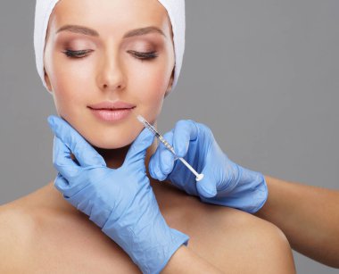 Genç bir kadının güzel yüzüne iğne yapan bir doktor. Estetik ameliyat, cilt gerdirme ve estetik tıp konsepti.