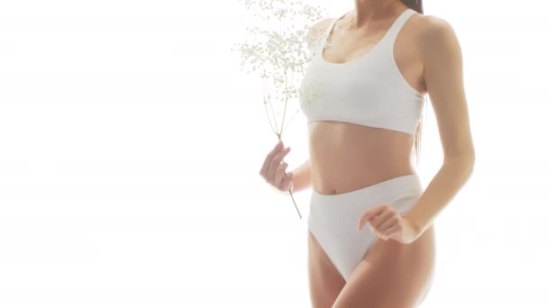 美丽的女人穿着白色内裤 在孤立的白色背景上抱着白花 演播室录象 关于身穿泳衣的健康少女 健康和皮肤护理 节食和化妆品的概念 — 图库视频影像