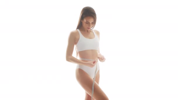 白い下着の美しい女性は 隔離された白い背景上のテープ測定を使用しています 水着の健康な若い少女の垂直スタジオビデオ 健康とスキンケア ダイエット 化粧品のコンセプト — ストック動画