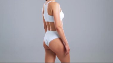 Genç, fit ve beyaz mayo giymiş güzel sarışın kadın gri arka planda poz veriyor. Sağlık, diyet, spor ve spor kavramı.