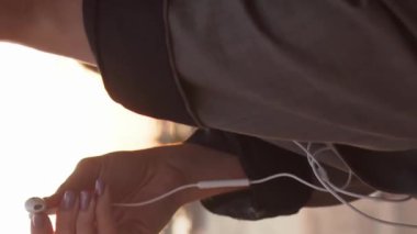 Genç çekici iş kadını dışarıda bankta oturuyor ve akıllı telefon kullanıyor. Gün batımı ışığı. Dikey video.