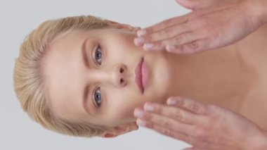 Cilt bakımı kremi süren genç, güzel ve doğal sarışın kadının stüdyo portresi. Dikey video. Yüz gerdirme, kozmetik ve makyaj konsepti.