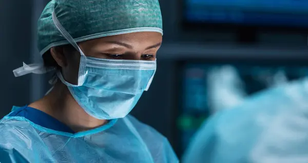 医療従事者の多様なチームは ハイテク機器と技術を使用して現代の手術室で外科手術を行います 外科医は病院で患者を救うために働いている ストック画像